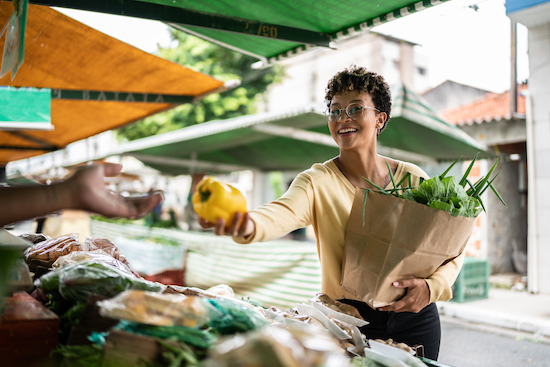 Mujer joven sonriendo comprando un pimiento amarillo en el mercado ambulante