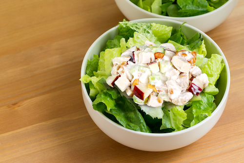 Green salad topped with prepared chicken salad in white bowl