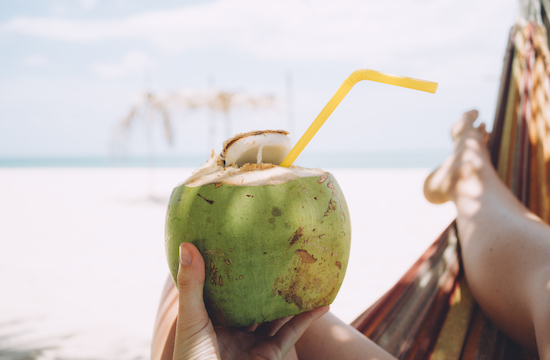 Mano sosteniendo un coco con un sorbete en la playa soleada