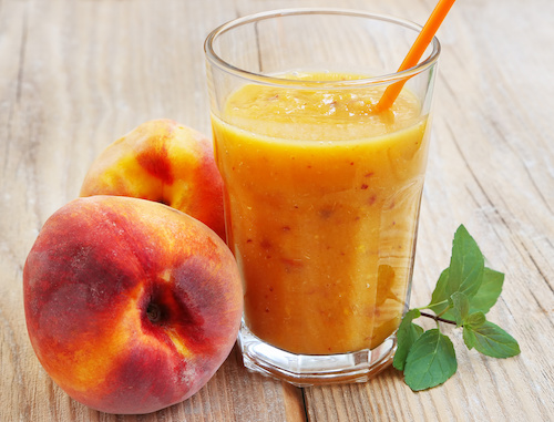 Batido de melocotón en vaso con popote naranja junto a melocotones frescos
