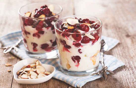Dos parfaits de yogur de cereza y almendras en tazas de cristal pequeñas