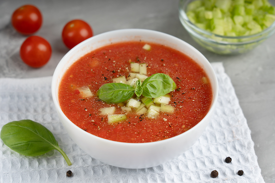 Gazpacho de tomate y frijoles blancos en tazón blanco decorado con albahaca fresca