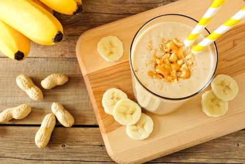 Batido de mantequilla de maní y banana en vaso de vidrio con popote amarillo
    