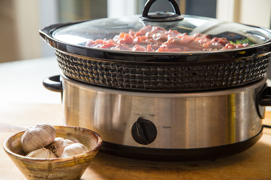 Olla de cocción lenta grande llena de carne de pollo para tacos junto a cabezas de ajo fresco