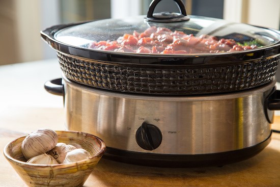 Large Slow Cooker Filled with Chicken Taco Meat Next to Fresh Garlic Bulbs