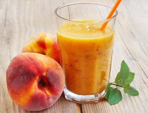 Peach Smoothie in Glass cup witn Orange Straw Next to Fresh Peaches