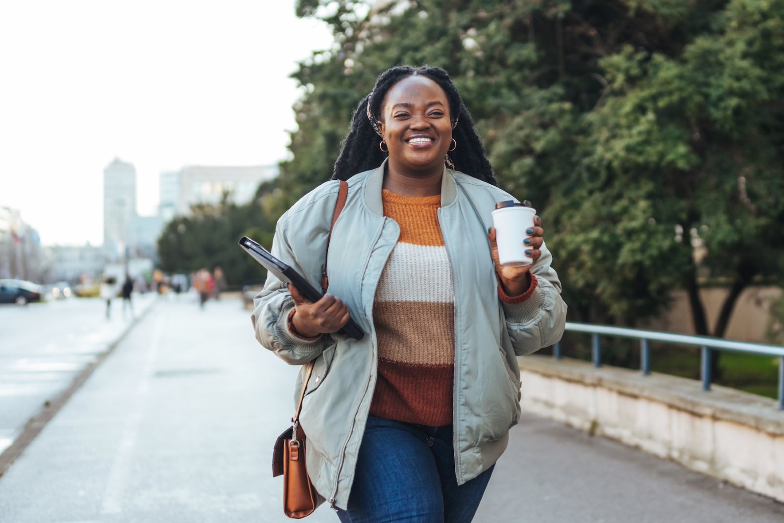 Une personne marchant sur un trottoir tenant une tasse et une tablette

Description générée automatiquement